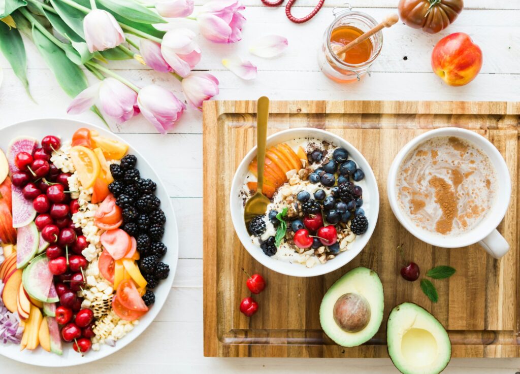 Bowl of fruit and oatmeal, fruit plate and Chai with a bouquet of pink tulips nearby 
